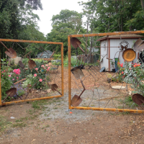 An artistic gate, slightly ajar, leading to the community garden.